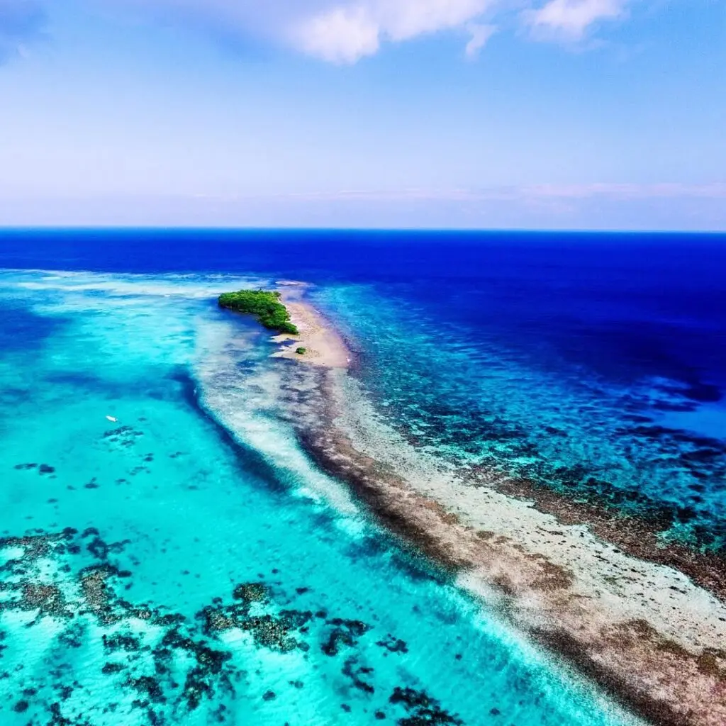 Photo of an island in Turneffe Atoll, Belize, with light blue shallow waters on one side and darker blue ocean waters on the other