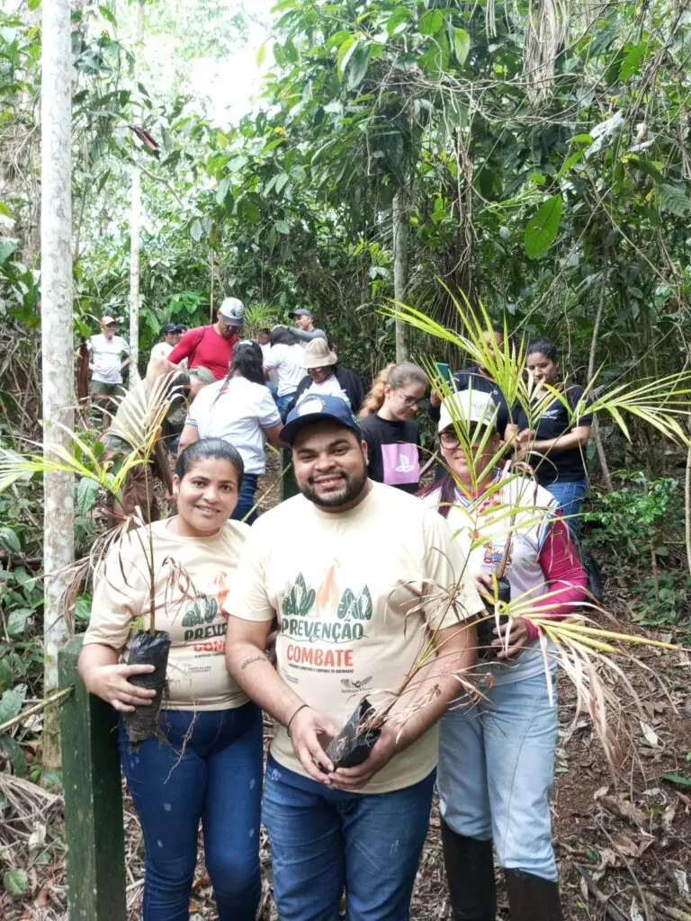 Photo of a group of people holding palm saplings as part of a restoration program for Serra Bonita reserve in Brazil