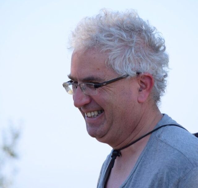 Profile of man with short white hair and wearing glasses, smiling