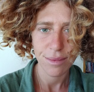 Portrait of a white woman with light brown curly hair, wearing a green shirt.