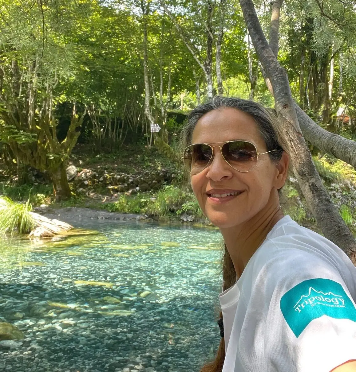 Close up photo of woman wearing sunglasses with a river and forest in the background