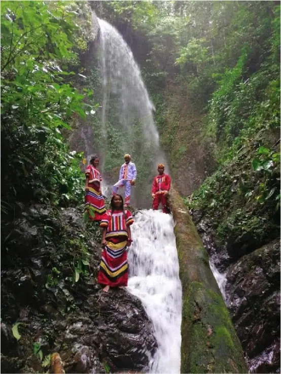 Photo of Indigenous Higa-onon people dressed in red traditional clothing standing beside a waterfall in the forest of Mount Sagyaan, Philippines.