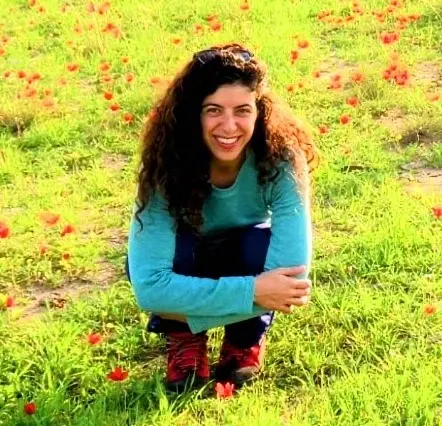 Picture of a woman with long dark hair crouched in a field of flowers